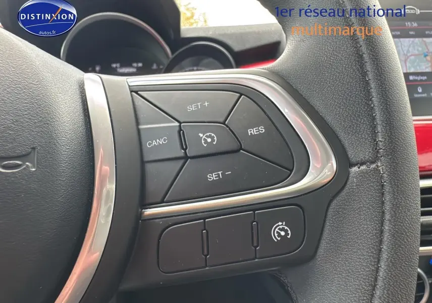 Gros plan sur les commandes du régulateur de vitesse au volant cuir noir de la FIAT 500X rouge 2020.