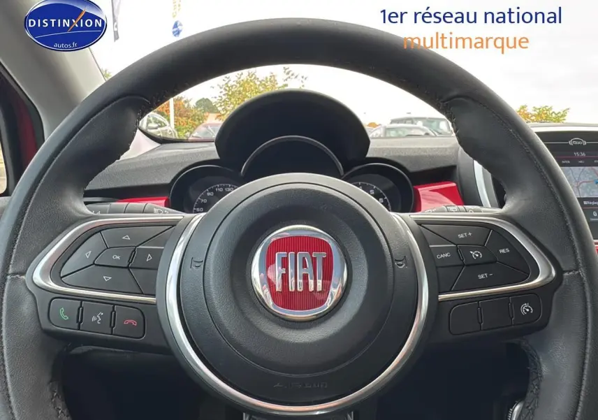 Vue rapprochée du volant cuir multifonction de la FIAT 500X rouge, avec commandes intégrées et tableau de bord visible.