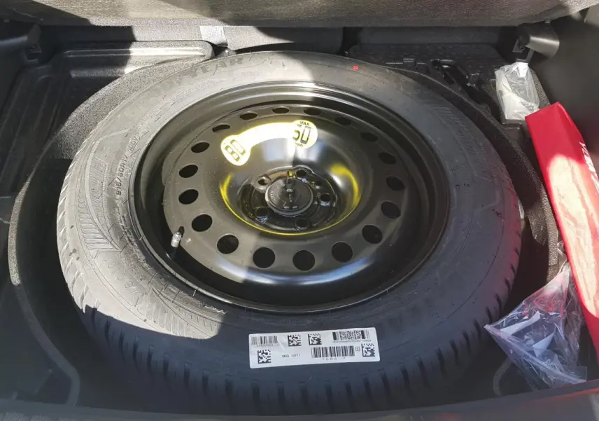 Vue plongeante sur la roue de secours noire dans le coffre du Jeep Compass blanc 2024, avec kit de secours rouge à côté.