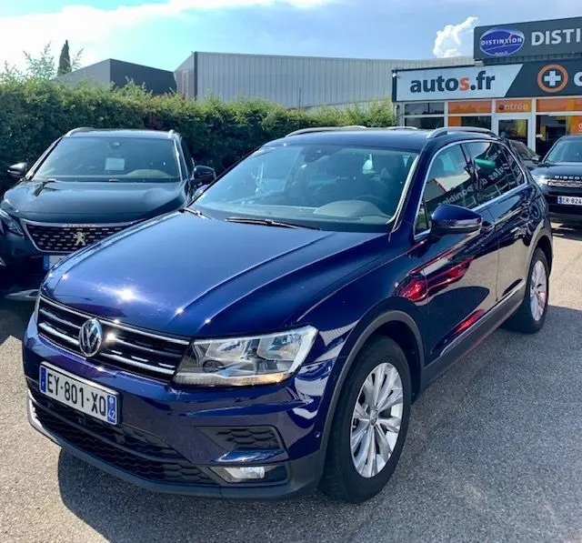 Volkswagen Tiguan bleu 3/4 avant droit, version 2.0 TDI 150ch Confortline Business 2018, garé devant un concessionnaire.