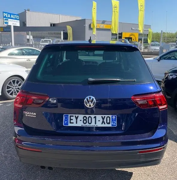 Vue arrière d'un Volkswagen Tiguan bleu foncé 2018 avec plaques françaises, stationné en extérieur près d'un concessionnaire Opel.