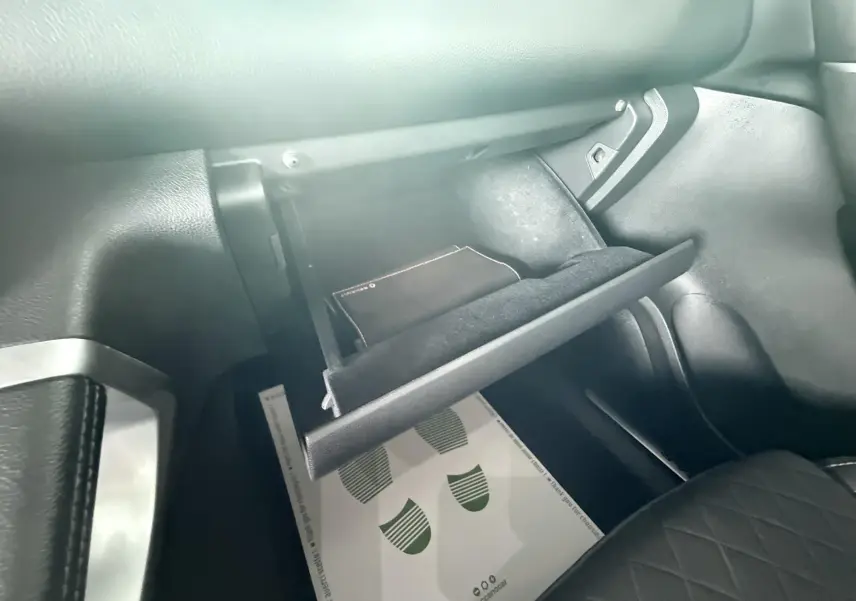 Gros plan sur la boîte à gants ouverte côté passager du Renault Kadjar gris, montrant un livret à l'intérieur.