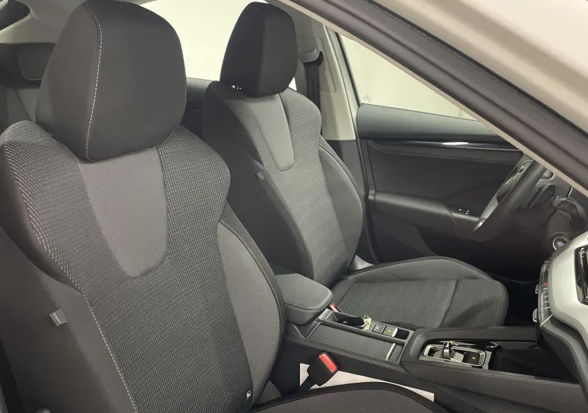 Vue intérieure côté conducteur de la Skoda Octavia 2024 blanc candy, montrant les sièges avant en tissu noir et la console centrale.