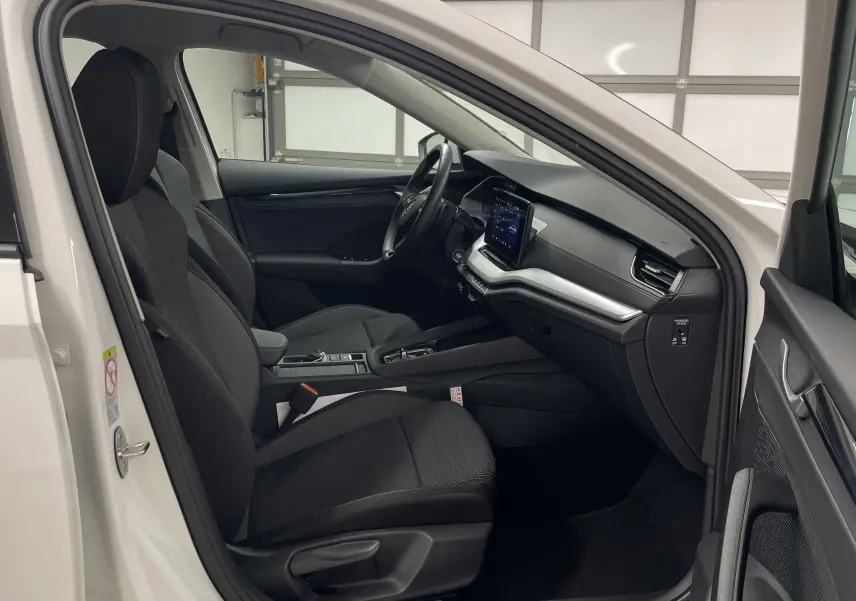 Intérieur côté conducteur d'une Skoda Octavia blanche 2024, sièges noirs et tableau de bord moderne avec écran tactile.