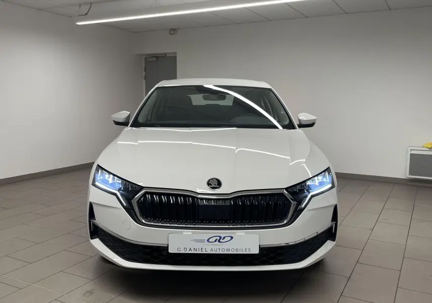 Vue de face d'une Skoda Octavia blanche Candy 2024 avec phares allumés dans un garage intérieur.