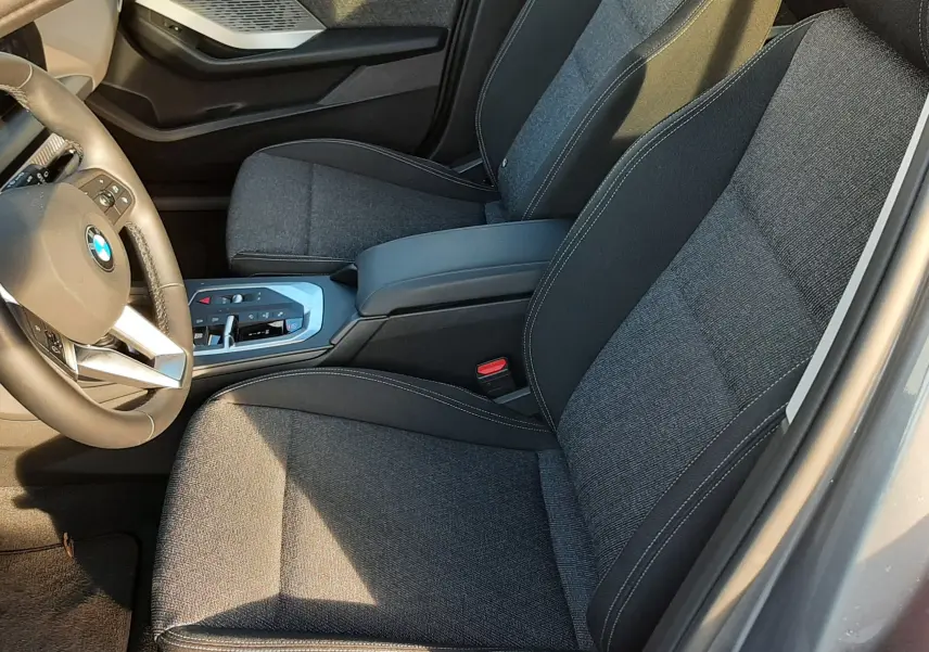 Vue intérieure côté conducteur de la BMW Série 1 gris Skyscraper, sièges tissu noir et console centrale moderne.