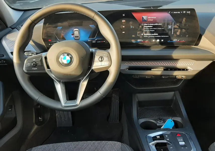 Intérieur BMW Série 1 2025 vue du conducteur, tableau de bord moderne avec écran digital et volant cuir noir.