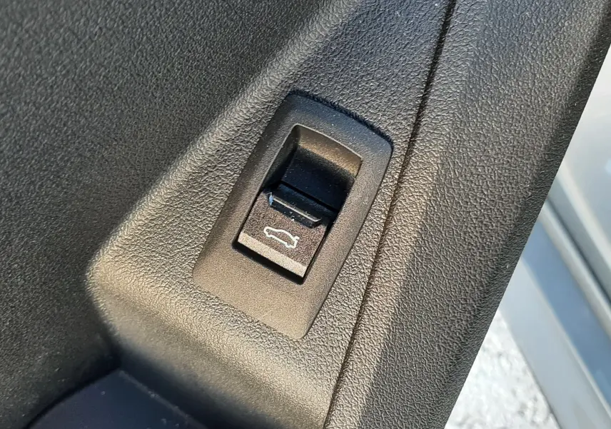 Bouton d'ouverture électrique du coffre sur la porte intérieure d'une BMW Série 1 gris Skyscraper, vue rapprochée.