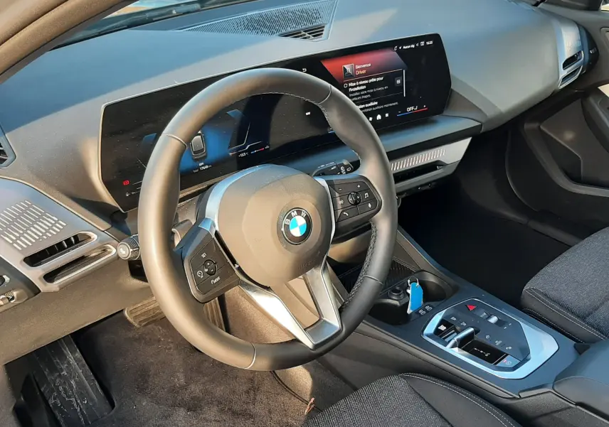 Vue intérieure côté conducteur de la BMW Série 1 120D 2025, tableau de bord numérique et volant multifonction noir.