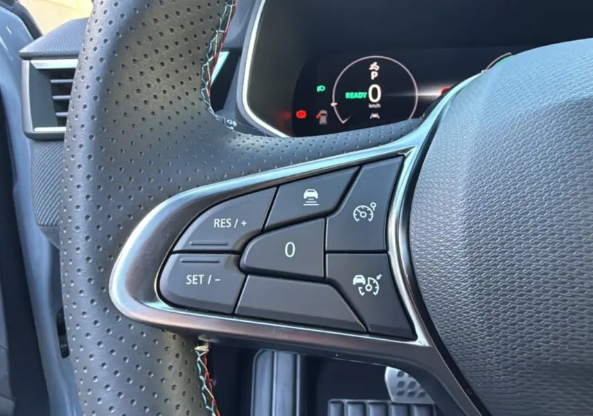 Gros plan sur les commandes au volant perforé de la Renault Clio V E-TECH 145 Esprit Alpine 2025, tableau de bord digital visible.