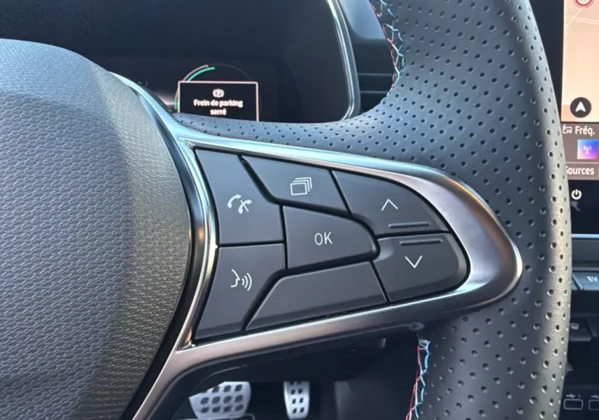 Gros plan sur les commandes au volant perforé de la Renault Clio V E-Tech 145 Esprit Alpine 2025, intérieur noir.