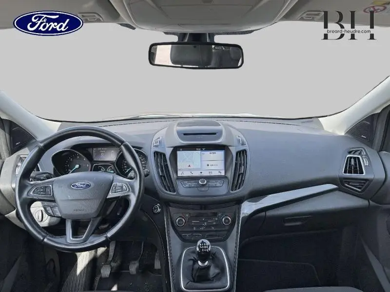 Vue intérieure avant du Ford Kuga 2017 avec tableau de bord noir, volant cuir multifonction et écran tactile central.