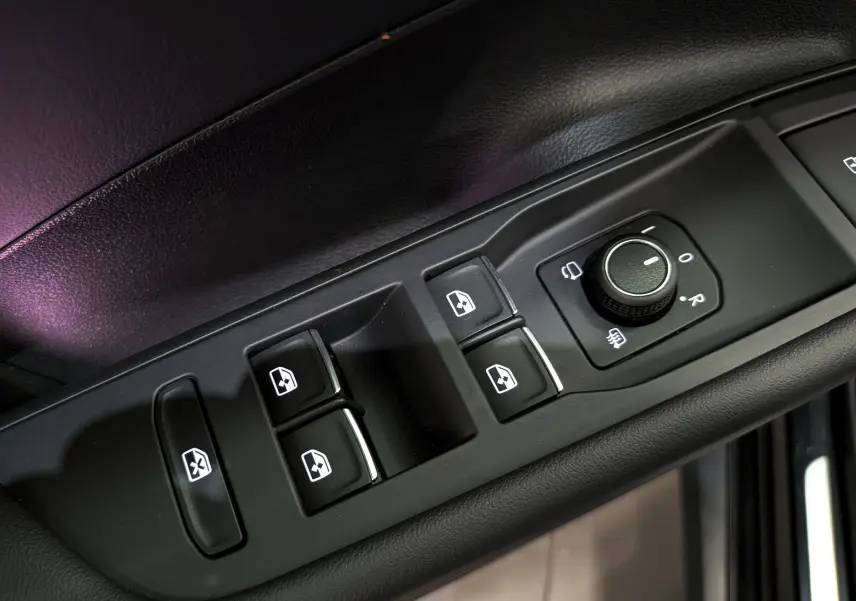 Gros plan sur les commandes de lève-vitres et réglage des rétroviseurs côté conducteur du Volkswagen T-Roc eTSI noir.