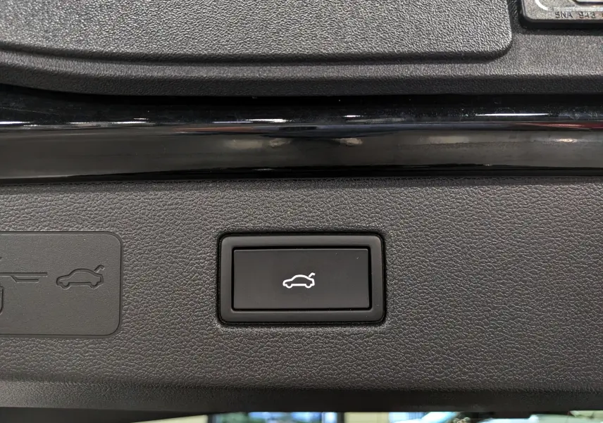 Bouton noir de commande d'ouverture électrique du coffre sur un Volkswagen T-Roc eTSI 150 CH DSG7 R-Line noir Ébène, vue intérieure.