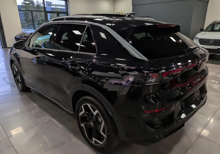 Vue 3/4 arrière droite du Volkswagen T-Roc eTSI 150 R-Line noir Ébène, avec jantes bi-ton et vitres teintées en showroom.