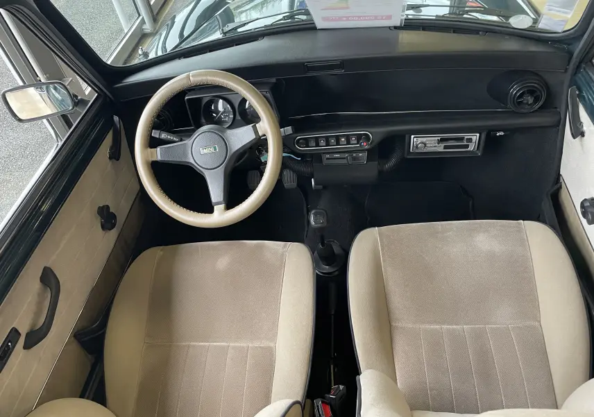 Vue intérieure avant du tableau de bord et des sièges beige clair d'une MINI 1.3 i British Open 1995 avec volant beige.