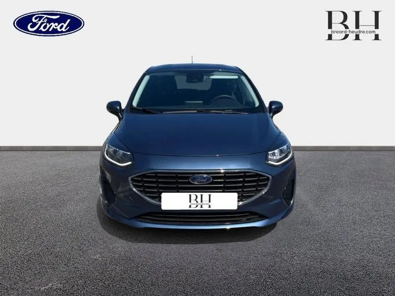 Vue frontale d'une Ford Fiesta 2022 bleu azur métallisé avec calandre chromée et phares LED allumés.