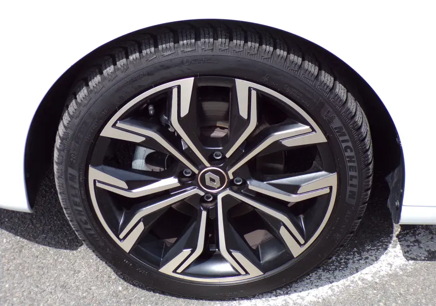 Gros plan sur la jante noire et argentée d'une Renault Clio V blanche, mettant en valeur le logo central Renault.