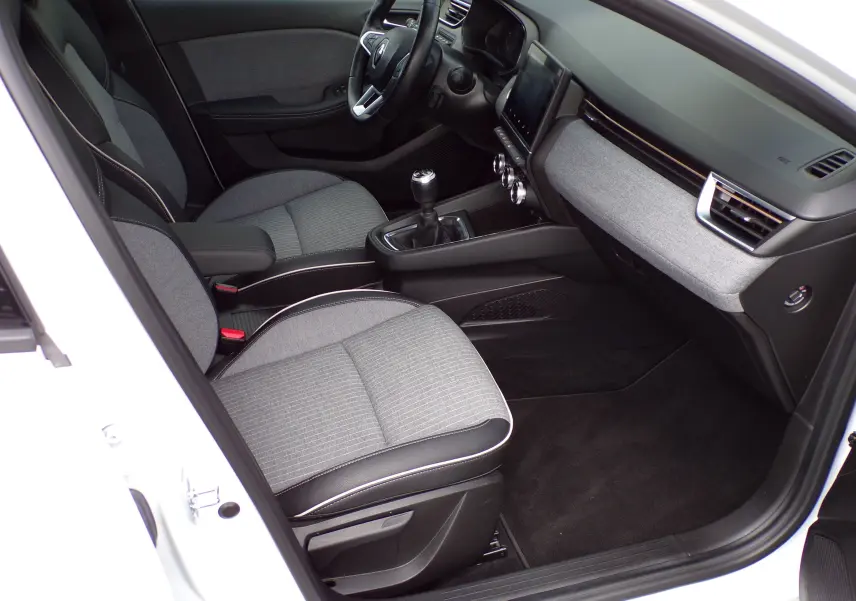 Vue intérieure côté conducteur de la Renault Clio V blanche 2022, sièges gris et tableau de bord moderne avec écran tactile.