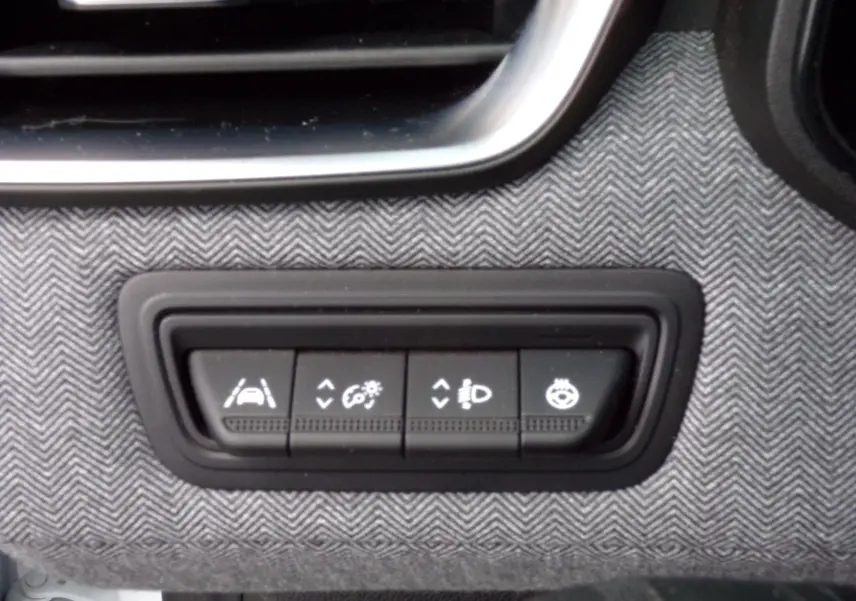 Gros plan sur les boutons de réglage d'assistance et éclairage intégrés dans la planche de bord tissu gris de la Renault Clio V blanche.