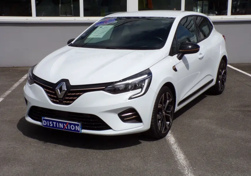 Renault Clio V blanche vue en 3/4 avant droit, avec jantes noires et détails de calandre cuivrés visibles.