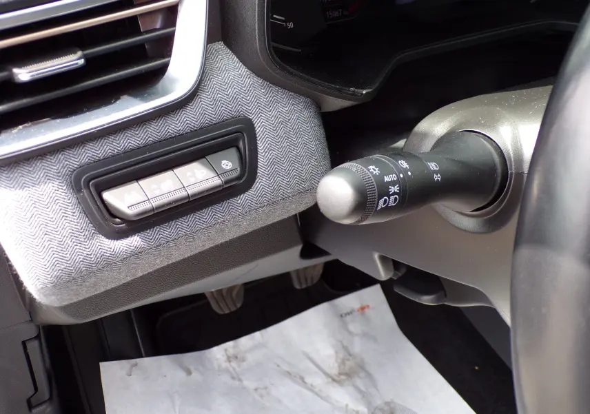 Gros plan sur la commande d'éclairage et les boutons de réglage à gauche du volant d'une Renault Clio V blanche, intérieur tissu gris.