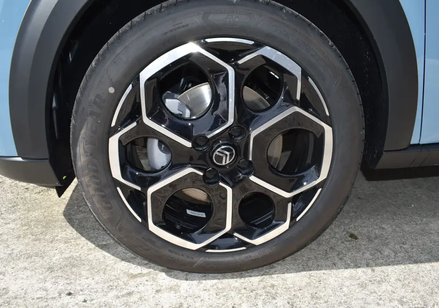 Gros plan sur la roue avant gauche d'une Citroën C3 2025 bleu toit noir avec jante noire et argentée au design hexagonal.