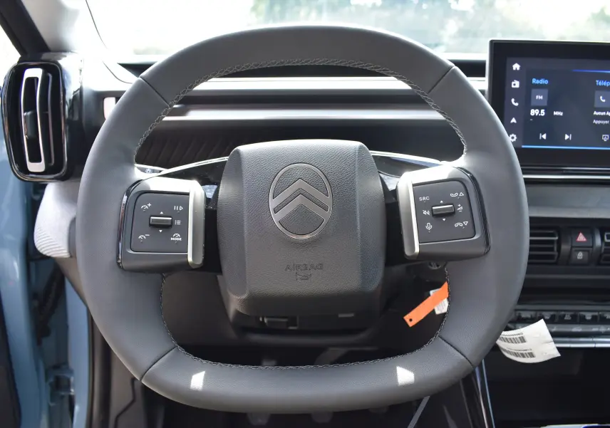 Vue rapprochée du volant cuir noir de la Citroën C3 2025 bleu toit noir, avec commandes intégrées et tableau de bord digital.