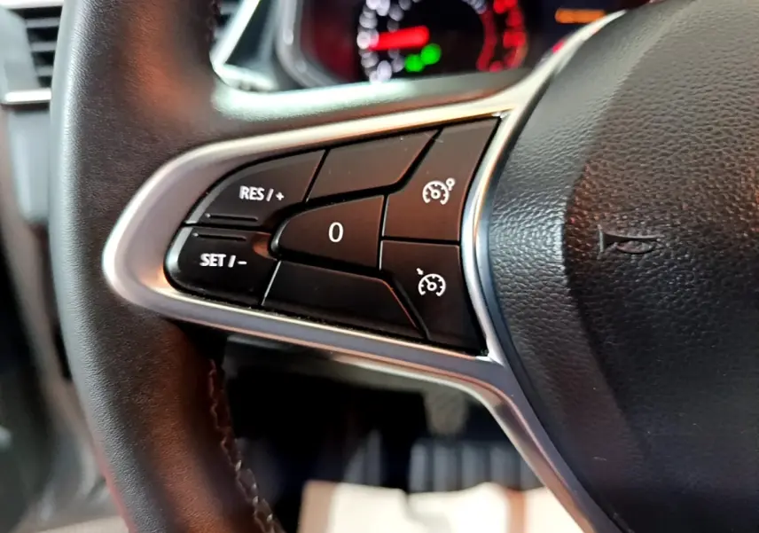 Gros plan sur les commandes du régulateur de vitesse à gauche du volant cuir noir de la Renault Clio gris clair 2023.