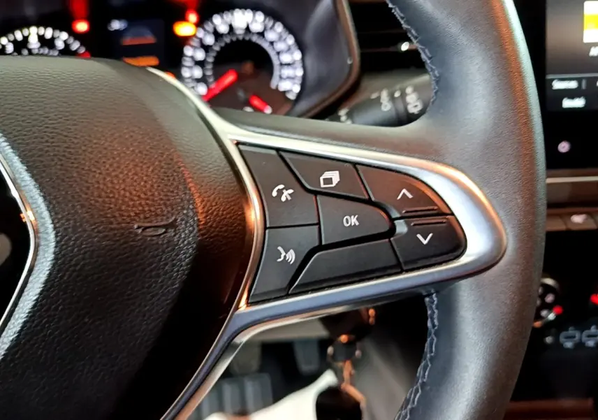 Gros plan sur le volant cuir noir côté gauche de la Renault Clio 2023 avec commandes multifonctions et tableau de bord lumineux.