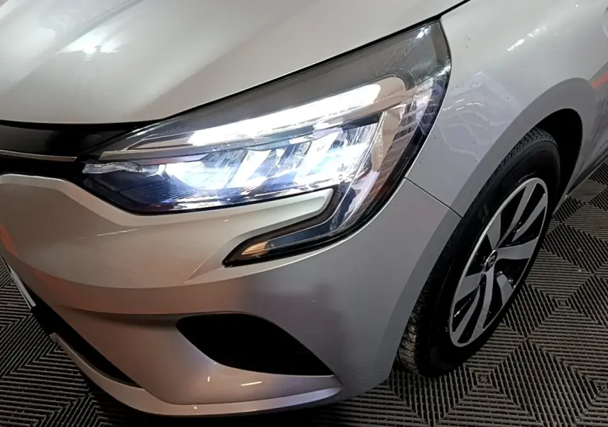 Gros plan sur l'avant droit gris clair de la Renault Clio 2023, mettant en valeur le phare LED et la jante design.
