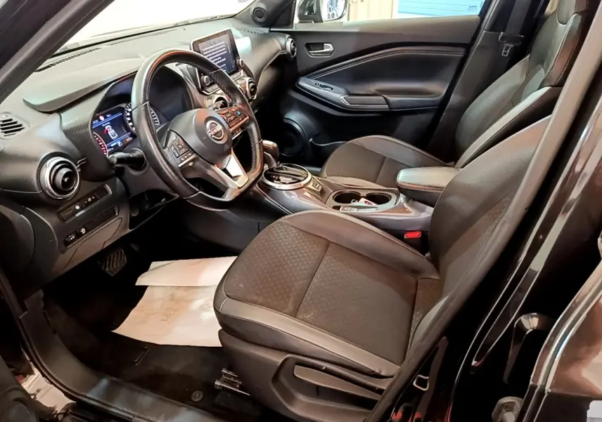Vue intérieure côté conducteur du Nissan Juke noir 2022, montrant sièges, volant multifonctions et écran tactile central.