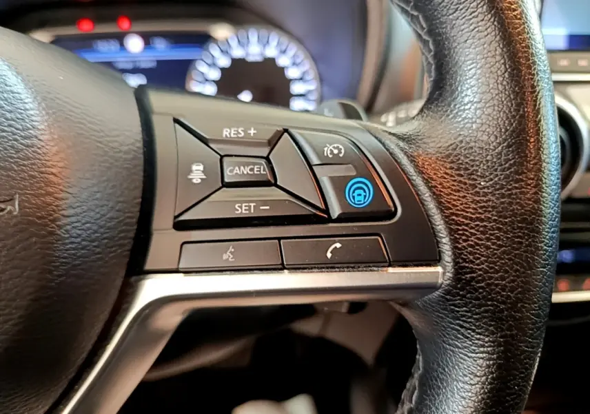 Gros plan sur les commandes du volant noir du Nissan Juke 2022, avec affichage digital flou en arrière-plan.