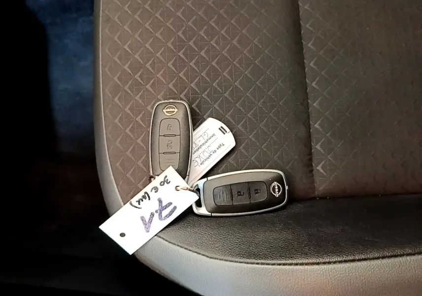 Gros plan sur deux clés Nissan posées sur un siège tissu noir à motifs géométriques à l'intérieur du véhicule.