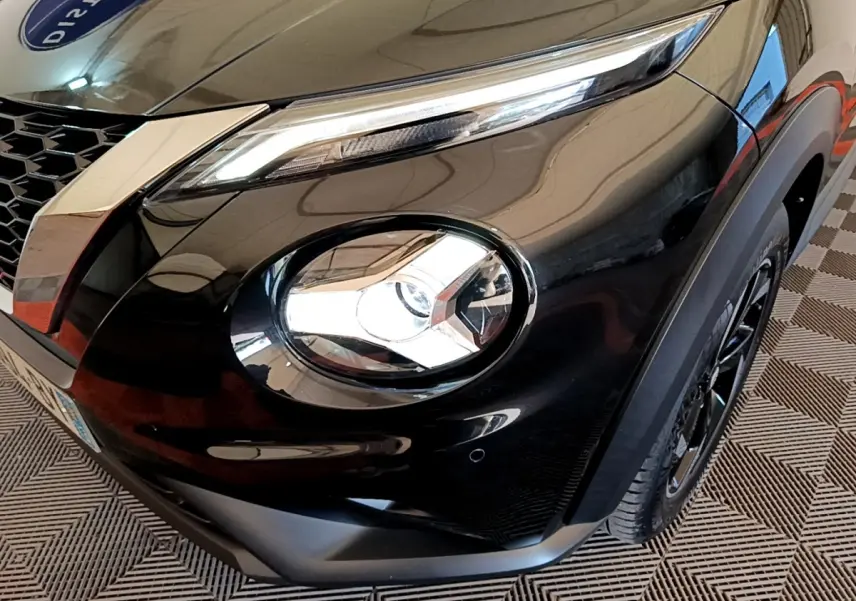 Gros plan sur l'avant droit noir brillant du Nissan Juke 2022, mettant en valeur son phare rond et son optique LED étirée.