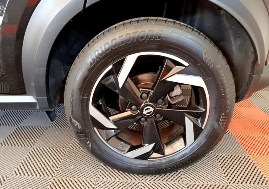 Gros plan sur la roue avant droite du Nissan Juke noir 2022 avec jante alliage bicolore et pneu Bridgestone.
