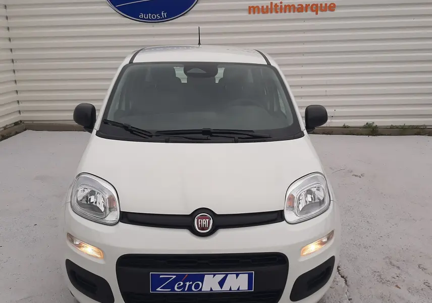 Vue frontale d'une Fiat Panda 2025 blanc gelato avec phares allumés et plaque Zéro KM visible.