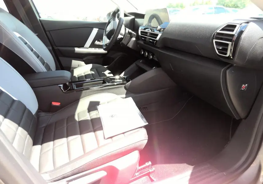 Vue intérieure côté passager avant de la Citroën C4 Hybrid 2025 avec sièges bi-ton gris et noir et tableau de bord moderne.