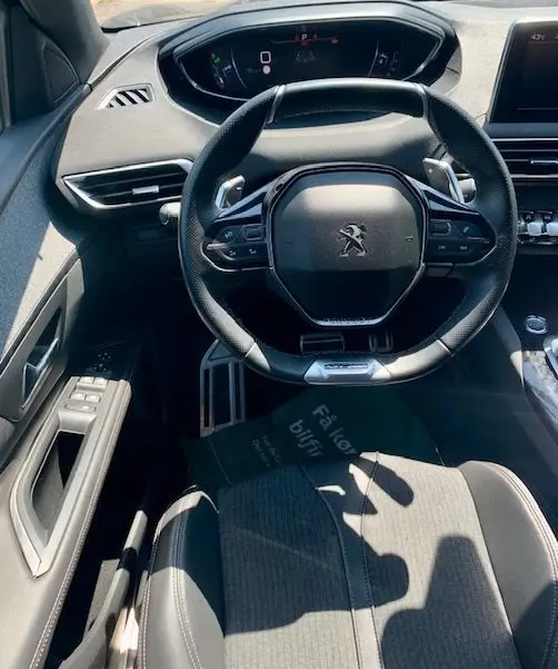 Vue intérieure centrée sur le volant compact du Peugeot 3008 noir 2018, avec tableau de bord numérique et commandes intégrées.