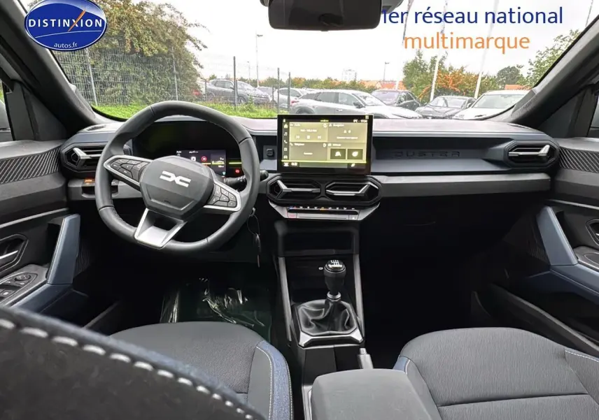 Vue intérieure avant du Dacia Duster 2025 avec tableau de bord moderne, écran tactile et volant multifonction noir.