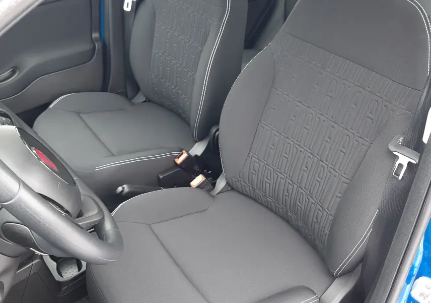 Vue intérieure côté conducteur de la Fiat Panda 2025 bleu Italia, sièges noirs avec motif FIAT embossé et coutures blanches.