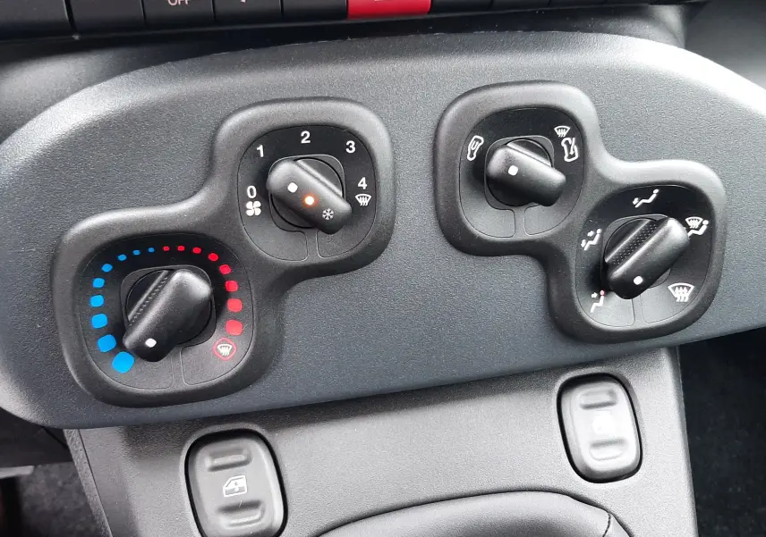 Commandes de climatisation et boutons de sécurité sur tableau de bord noir de la Fiat Panda 2025.