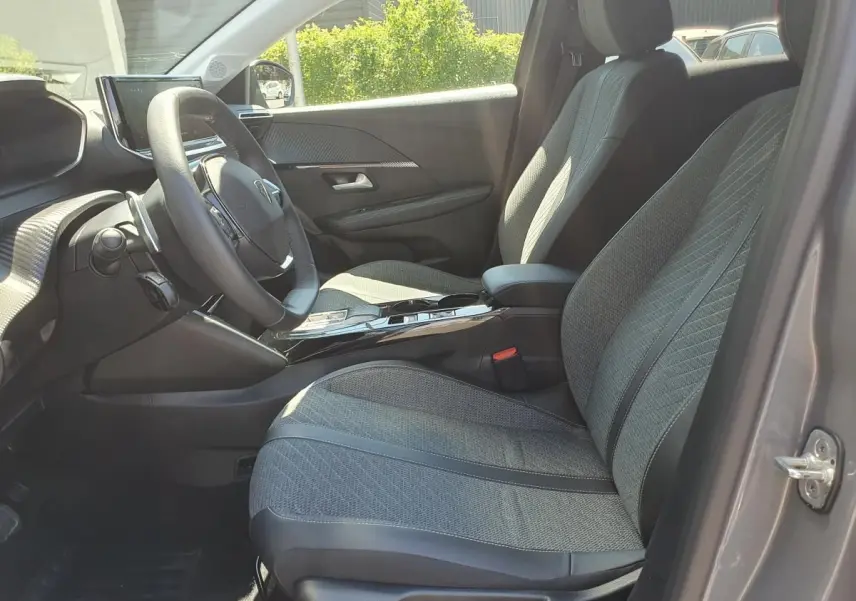 Vue intérieure côté conducteur de la Peugeot 208 1.2 Hybrid 110 Allure gris Sellenium, sièges tissu gris et console centrale brillante.