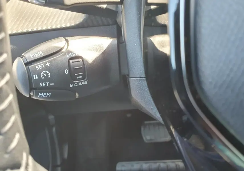Gros plan sur la commande de régulateur de vitesse à gauche du volant dans l’habitacle d’une Peugeot 208 gris Sellenium.