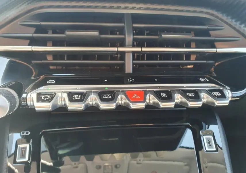 Vue rapprochée de la console centrale noire brillante avec boutons argentés et rouge dans une Peugeot 208 gris Sellenium.