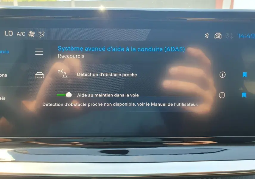 Écran tactile intérieur affichant le menu d’aide à la conduite du Peugeot 208 hybride, avec reflet des mains.