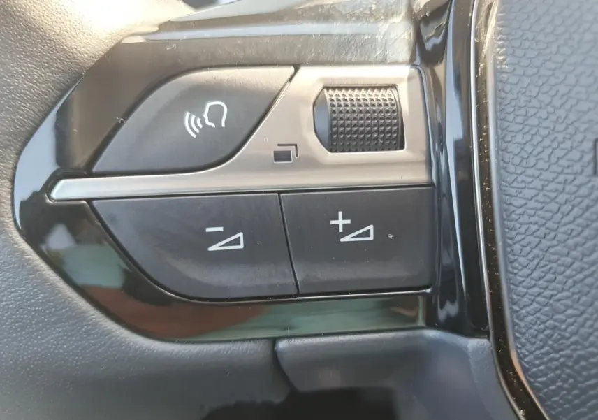 Gros plan sur les commandes de volume et de reconnaissance vocale sur le volant noir du Peugeot 208 gris Sellenium 2025.