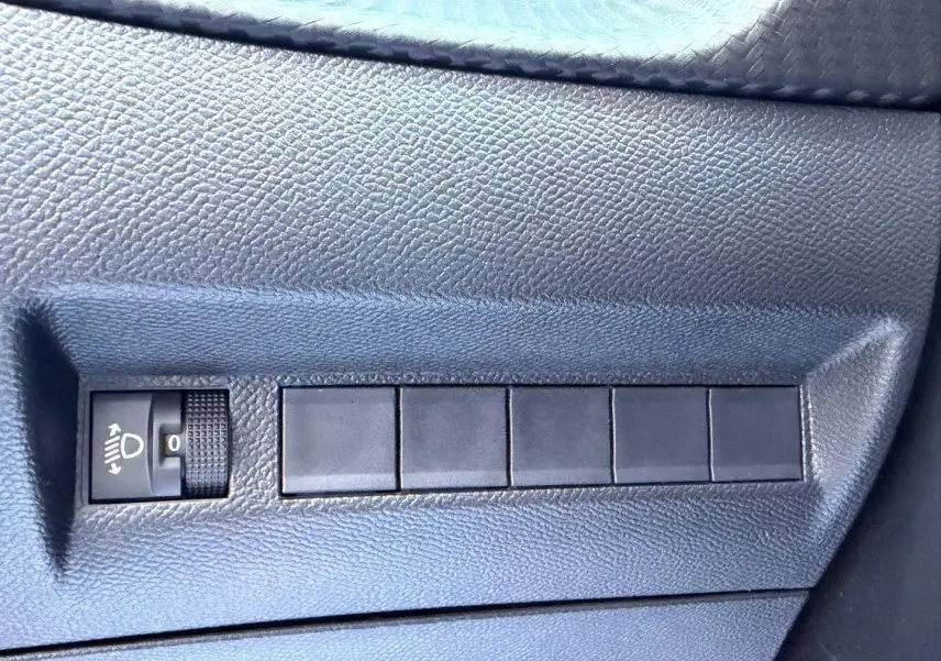 Gros plan sur le bouton de réglage des phares dans l’habitacle noir du Peugeot 208 jaune 2025.