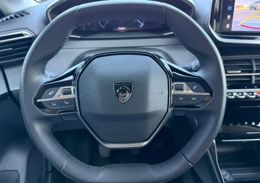 Vue rapprochée du volant cuir noir de la Peugeot 208 2025 avec commandes intégrées et écran tactile visible à droite.