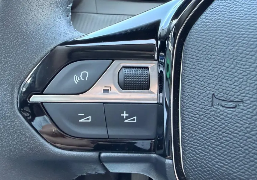 Gros plan sur les commandes audio noires et argentées situées sur le côté gauche du volant en cuir noir.